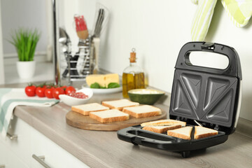 Modern sandwich maker with bread slices on wooden table in kitchen - obrazy, fototapety, plakaty