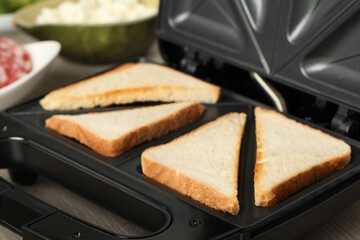 Modern sandwich maker with bread slices on wooden table, closeup