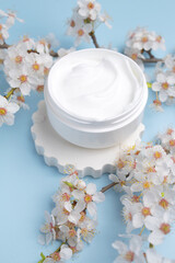 Container with bodycare and skincare cream on a blue background with blooming cherry. Cosmetic facial skin care and spa. Natural treatment concept.
