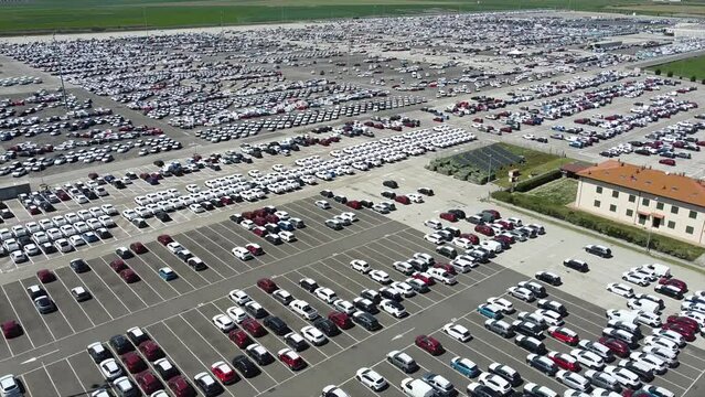 Italy, April 2022 , Aerial view of new cars parked in car parking. Car dealer parking lot full of new automobiles. New cars lined up for import and export business - green revolution and electric car