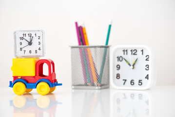 there is a clock on a bright colored car, a glass with pencils next to it, and a square clock