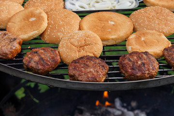 Homemade crispy fried hamburger patties on the grate of a charcoal grill over glowing coals with small flames