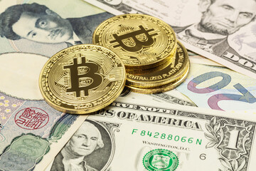Four cryptocurrency coins laid on top of US Dollar, Yen and Euro banknotes