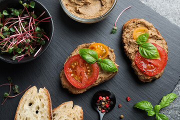 Slices of bread with delicious pate, tomatoes and basil on grey table, flat lay