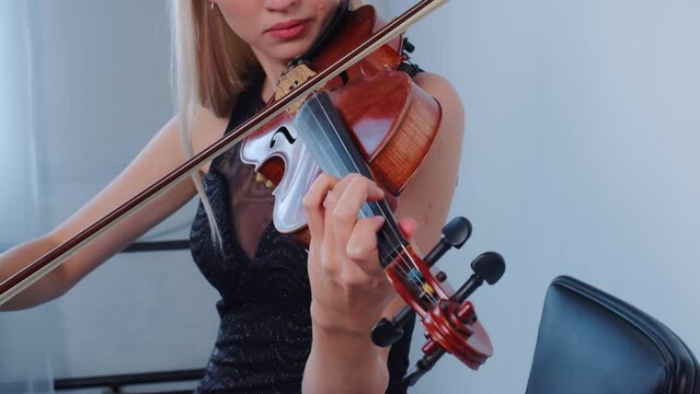Beautiful violinist playing violin with inspiration indoor. Blonde young woman is learning melody. Female european fiddler rehearsing before exam, concert, performance. Hobby, music, fiddle. Close up