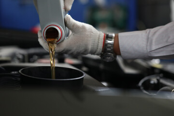 Auto mechanic refueling and pouring oil into engine motor ia car