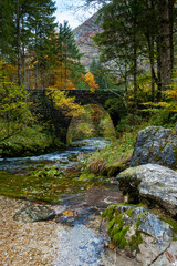 Mountain stream of clear fresh water passing under a stony bridge in autumnal landscape