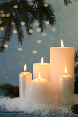 Burning candles with fir tree branch, cones and artificial snow on blue wooden table. Christmas atmosphere