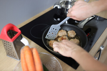 Man frying meat balls in pan on kitchen stove