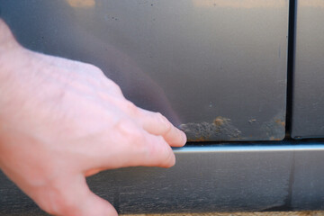 Close-up, selective focus on rust and hand. A man shows rust on a car door from winter reagents. The concept of harm from reagents for the environment