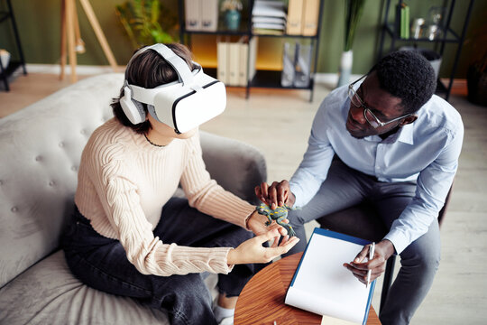 Therapist Giving Toy Frog To Young Patient Wearing Virtual Reality Headset And Asking To Describe Feelings