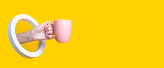 Female hand holding a pink cup in a round hole on a yellow background. Banner.