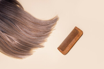 Wig light blond ash, wooden comb on a beige background. Top view, flat lay.