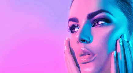 Fototapeten High Fashion model girl face in colorful bright UV lights in studio, portrait of beautiful woman with trendy make-up and manicure. Art design, colorful make up. Over colourful purple, blue background © Subbotina Anna