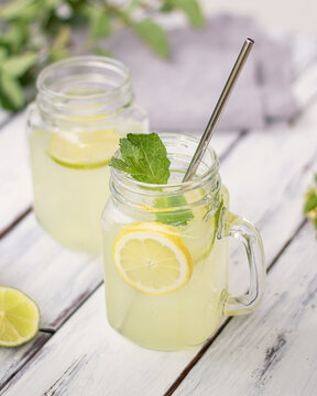 Two mugs with lemon and lime lemonade on white table