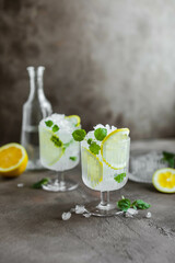Two beautiful glasses with a cooling citrus drink. Lemonade with lemon, mint and crushed ice.