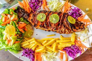 Spicy grilled fish served with french fries and salad