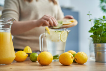 Lemons in the foreground and unrecognizable person making homemade lemonade with fresh