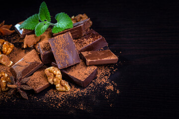 A pile of dark broken chocolate sprinkled with cocoa powder, nuts and spices. Copy space