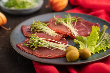 Slices of smoked salted meat with cilantro microgreen on black. Side view, selective focus.