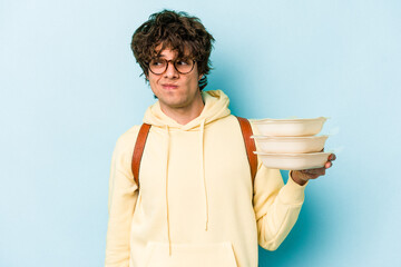 Young caucasian student man holding a tupperware isolated on blue background confused, feels...