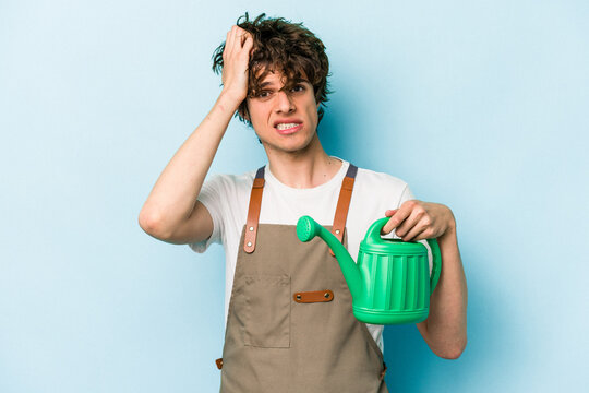 Young gardener caucasian man holding watering can isolated on blue background being shocked, she has remembered important meeting.