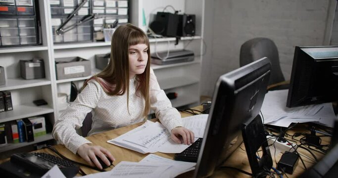 A young tired woman works in the office at the computer and fight sleep. A woman reading a text on paper and looks at the computer. Slow-motion 4k footage