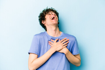 Young caucasian man isolated on blue background laughing keeping hands on heart, concept of happiness.