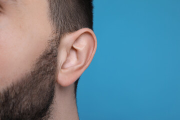 Fototapeta premium Man on light blue background, closeup of ear. Space for text
