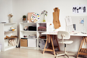 Desk and shelves with sewing patterns, various fabric and fashion sketches in tailoring atelier
