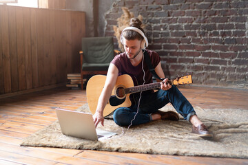 Man acoustic guitar sitting floor with laptop and headphones playing singing song online music...