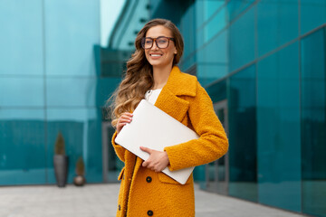 Business woman with laptop dressed yellow coat standing outdoors corporative building background