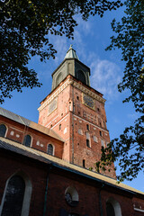 Naklejka premium The tower of Turku Cathedral, the medieval basilica in Finland against blue sky in summer with trees in the foreground