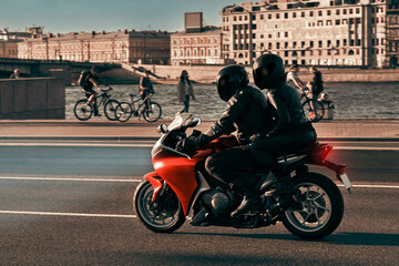 A man and a woman ride together on a sports motorcycle along the embankment. Motorcyclists drive around the city in the evening on a red sports bike.Headlights at night.