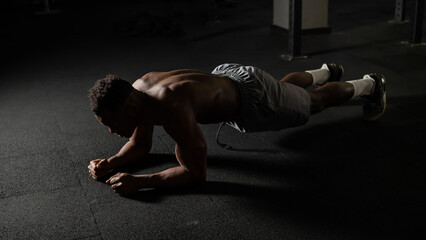 Shirtless african american man doing an elbow plank in the gym.