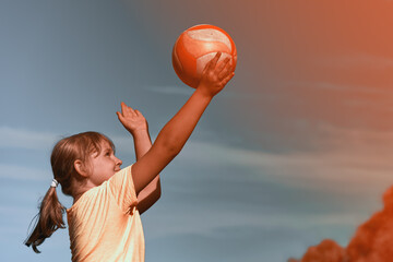 A girl is playing volleyball . The child hits the ball with his hand . Outdoor play