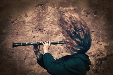 Street musician playing classical music in the street. The girl plays the clarinet in a strong wind. Classical musician outdoor. - obrazy, fototapety, plakaty