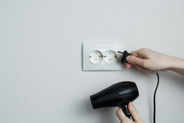 the girl connects the hair dryer to the electrical network.