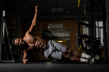 Fototapeta na wymiar Shirtless african american man doing an elbow side plank in the gym.