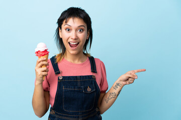 Young Uruguayan girl holding a cornet ice cream over isolated blue background surprised and...