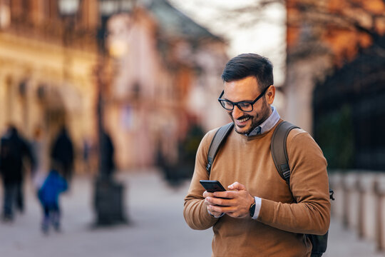 Cheerful caucasian man with backpack on, browsing the internet on his mobile.