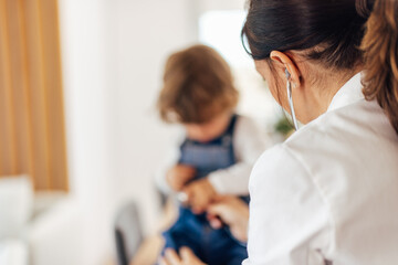 Fototapeta premium Focus on the female brunette pediatrician, and male toddler sitt