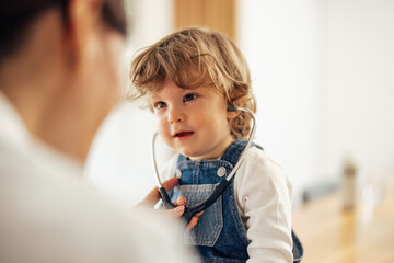 Close up of a cute toddler, trying on a stethoscope with a docto