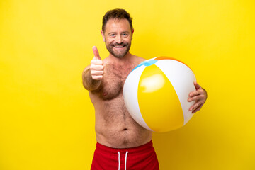 Middle age caucasian man holding beach ball isolated on yellow background with thumbs up because...