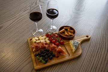 wood plate with prosciutto, meat, cheese, tomato cherry, olives, snack and wine glasses 