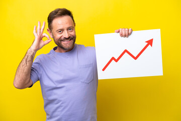 Middle age caucasian man isolated on yellow background holding a sign with a growing statistics arrow symbol with ok sign