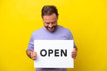 Middle age caucasian man isolated on yellow background holding a placard with text OPEN