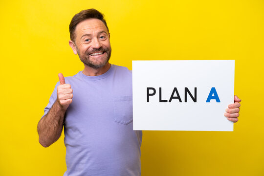 Middle age caucasian man isolated on yellow background holding a placard with the message PLAN A with thumb up