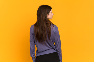 Young Ukrainian girl isolated on yellow background in back position and looking side