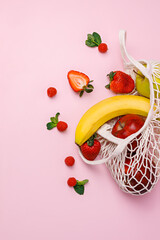 Fruit in the crochet shopping bag on pastel pink background. Creative food concept. Tropical summer...